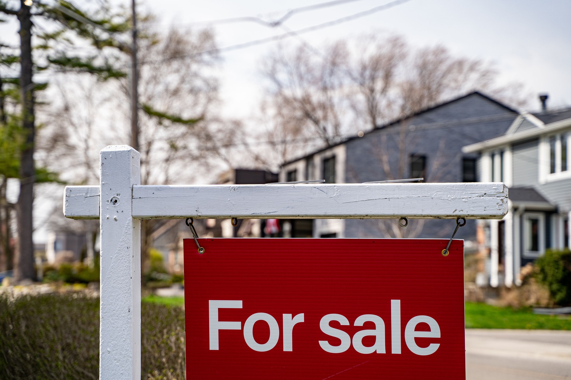 Sign of a for sale board in front of a house on the street.